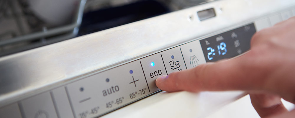 Close-up of an appliance's control panel and someone pressing the "eco" button.