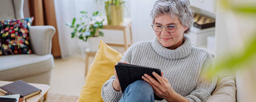 Woman lounging on couch reading on a tablet.