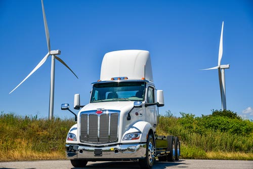 Peterbuild EV truck parked in front of wind turbines with blue skies in the background.